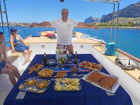 A cheerful host presents a delicious spread of snacks and drinks on a boat, perfect for a fun day at sea with friends.