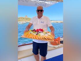 A smiling host presents a vibrant fruit platter aboard a boat, showcasing fresh and colorful selections perfect for a luxurious day on the water.
