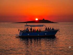 A group enjoys a stunning sunset aboard a boat, with an island silhouette in the background — a perfect moment for celebration on the water.