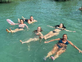 A lively group of friends enjoys a refreshing swim, floating together in clear turquoise waters — a perfect moment of relaxation and fun under the sun.