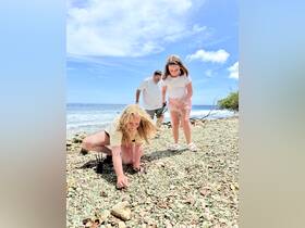 A family enjoys a day at the beach, with children exploring the shoreline and discovering treasures among the pebbles — a perfect moment of adventure and bonding by the ocean.