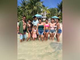 A joyful family poses together in shallow water at the beach, enjoying a sunny day surrounded by palm trees — perfect for memorable family vacations.