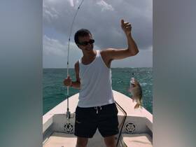 A man proudly displays his catch while fishing on a boat, showcasing the thrill of ocean adventures and the joy of reeling in a big one.