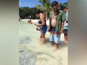 A group of people, including a child, interacts with stingrays in shallow water, creating a memorable wildlife experience in a tropical setting.
