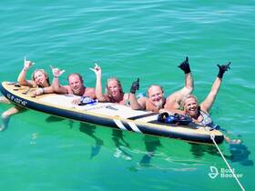 A lively group enjoys a fun day on the water, paddleboarding and celebrating in the vibrant turquoise sea — perfect for summer adventures.