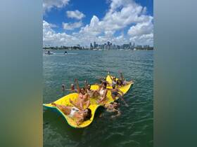 A lively group enjoys a fun day on a floating mat in the water, with the stunning Miami skyline in the background — perfect for summer celebrations and group outings.
