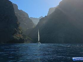 A sailboat navigates through a stunning coastal canyon, showcasing the breathtaking scenery of the surrounding cliffs and ocean — a perfect backdrop for sailing adventures.