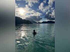 A serene scene of a person swimming in clear waters under a stunning sunset, surrounded by lush mountains — perfect for capturing the beauty of nature during a boating adventure.