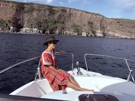 A woman enjoys a sunny day on a boat, smiling as she takes in the beautiful ocean views and rocky cliffs — a perfect moment for relaxation and adventure.