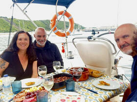 A joyful group enjoys a delicious meal aboard a sailboat, complete with wine and a scenic waterfront view — perfect for memorable dining experiences on the water.