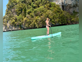 A woman paddleboards in serene turquoise waters, surrounded by lush cliffs — a perfect snapshot of adventure and natural beauty.