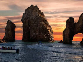 A scenic sunset view featuring iconic rock formations and a boat with guests cruising in the ocean — a perfect highlight of a coastal adventure.