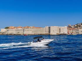 A speedboat glides through the vibrant waters near Dubrovnik, showcasing the stunning coastline and historic architecture in the background — perfect for exploring the Adriatic Sea.