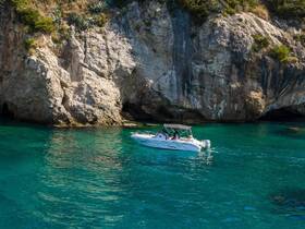 A scenic view of a boat navigating through crystal-clear waters near a rocky coastline, perfect for exploring hidden coves and enjoying the beauty of nature.