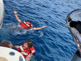 Two friends enjoy a refreshing swim in the open water, showcasing the fun and excitement of a day on the boat with life jackets for safety.