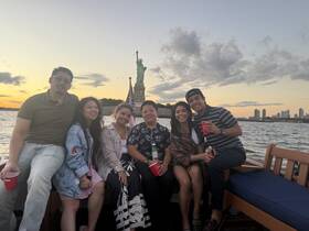 A lively group enjoys a sunset cruise near the Statue of Liberty, celebrating with drinks and smiles — a perfect backdrop for memorable moments on the water.
