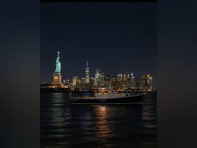 A serene night view of a boat gliding past the Statue of Liberty, with the stunning New York City skyline illuminated in the background — a perfect scene for evening cruises.