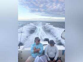 Two friends relax on a boat while enjoying a day of fishing, with the scenic water and sky in the background — perfect for a day out on the water.