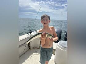 A young boy proudly holds up his catch of the day while fishing on a boat, showcasing the joy of a successful fishing trip.