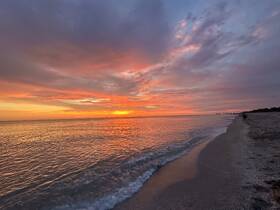 A stunning sunset casts vibrant colors over the tranquil beach, creating a picturesque coastal scene perfect for evening strolls and relaxation.