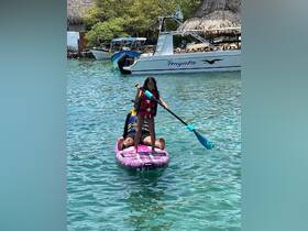 A young girl paddleboards with an adult in clear turquoise waters, showcasing a fun and adventurous water activity perfect for family outings.