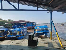 A vibrant blue boat docked at a riverside, showcasing its structure against a scenic backdrop of water and greenery.