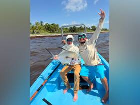 Two anglers celebrate their successful catch aboard a boat, showcasing a beautiful fish against a tropical backdrop — a perfect moment for fishing enthusiasts.