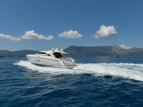 A sleek yacht cruises through clear blue waters, showcasing its elegant design and powerful performance against a stunning mountainous backdrop.