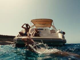 A lively scene captures friends enjoying a sunny day on the water, with one person swimming and others relaxing on the boat — perfect for summer adventures.