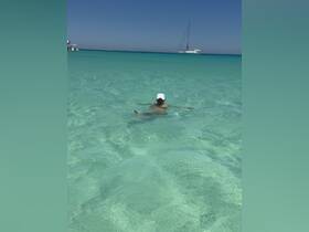 A child enjoys swimming in the crystal-clear waters with a sailboat in the background, capturing the essence of a perfect beach day.