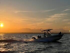 A group enjoys a sunset fishing trip on a boat, creating a picturesque scene with the sun setting behind the mountains — perfect for adventure seekers.