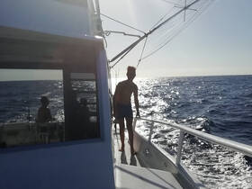 A young person stands on the deck of a boat, enjoying a sunny day on the ocean, with fellow passengers visible in the background — a perfect moment for fishing and adventure on the water.