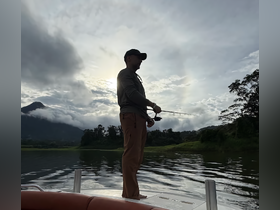 A fisherman casts his line into tranquil waters, surrounded by stunning mountain scenery — a perfect moment for fishing enthusiasts.