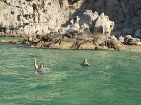 Two friends enjoy a refreshing swim in crystal-clear waters near a stunning rocky coastline, perfect for beach adventures and relaxation.