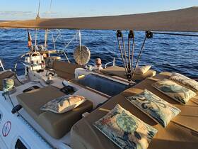 A cozy seating area on a sailboat, featuring decorative cushions and a helm, perfect for relaxing while enjoying the ocean views.