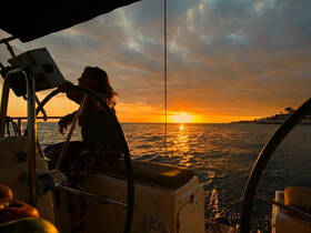 A silhouette of a woman at the helm of a sailboat during a stunning sunset, capturing the serene beauty of sailing on open waters.