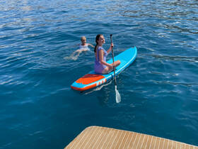 A girl paddleboards while a boy swims nearby in crystal-clear waters, capturing the essence of fun and adventure on a sunny day.
