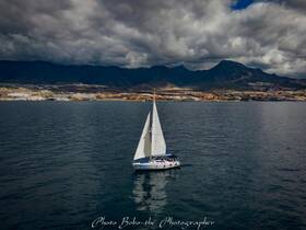 A stunning aerial view of a sailboat navigating calm waters with dramatic mountain scenery in the background, showcasing the beauty of sailing adventures.