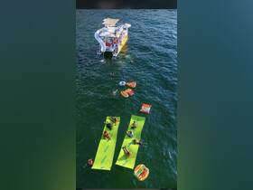 A lively group enjoys a fun day on the water with floating mats and a boat equipped with a slide, perfect for summer adventures and family outings.