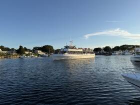 A lively boat, the 'Capt. John & Son,' navigates through a picturesque harbor filled with spectators enjoying the scenic views — perfect for a memorable cruise experience.