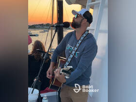 A musician performs live music on a boat during sunset, creating a perfect atmosphere for guests to enjoy the evening on the water.