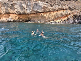 A group of friends enjoys a refreshing swim in crystal-clear waters near a stunning rocky coastline, perfect for adventure seekers and nature lovers.
