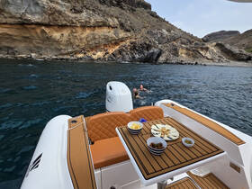 Guests enjoy a refreshing swim in the clear waters while snacks are laid out on the boat's table, showcasing a perfect day of relaxation and fun along the stunning coastline.