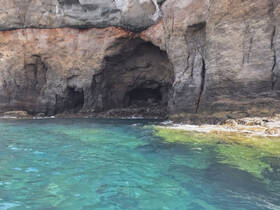 A stunning view of a rocky coastline featuring a cave, surrounded by crystal-clear turquoise waters — an ideal spot for exploration and adventure.