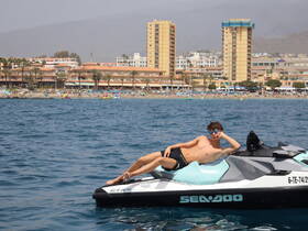 A young man relaxes on a jet ski, enjoying the summer sun with a beach backdrop — perfect for water sports enthusiasts looking for adventure.