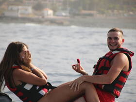 A joyful couple celebrates a romantic proposal on a boat, capturing a memorable moment against the backdrop of the ocean.