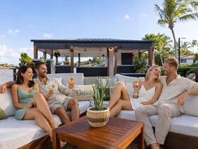 A joyful group enjoys cocktails on a stylish outdoor seating area, perfect for celebrations and social gatherings by the water.