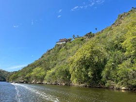 A scenic view of a hillside mansion overlooking a tranquil waterway, perfect for showcasing beautiful destinations during boat tours.
