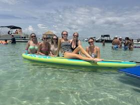 A fun group of friends enjoys a day at the beach, paddleboarding and relaxing in the clear waters — perfect for summer celebrations and beach parties.