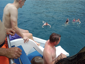 A lively scene of a group enjoying water activities, with some swimming and others preparing to jump from the boat — perfect for family fun in the sun.